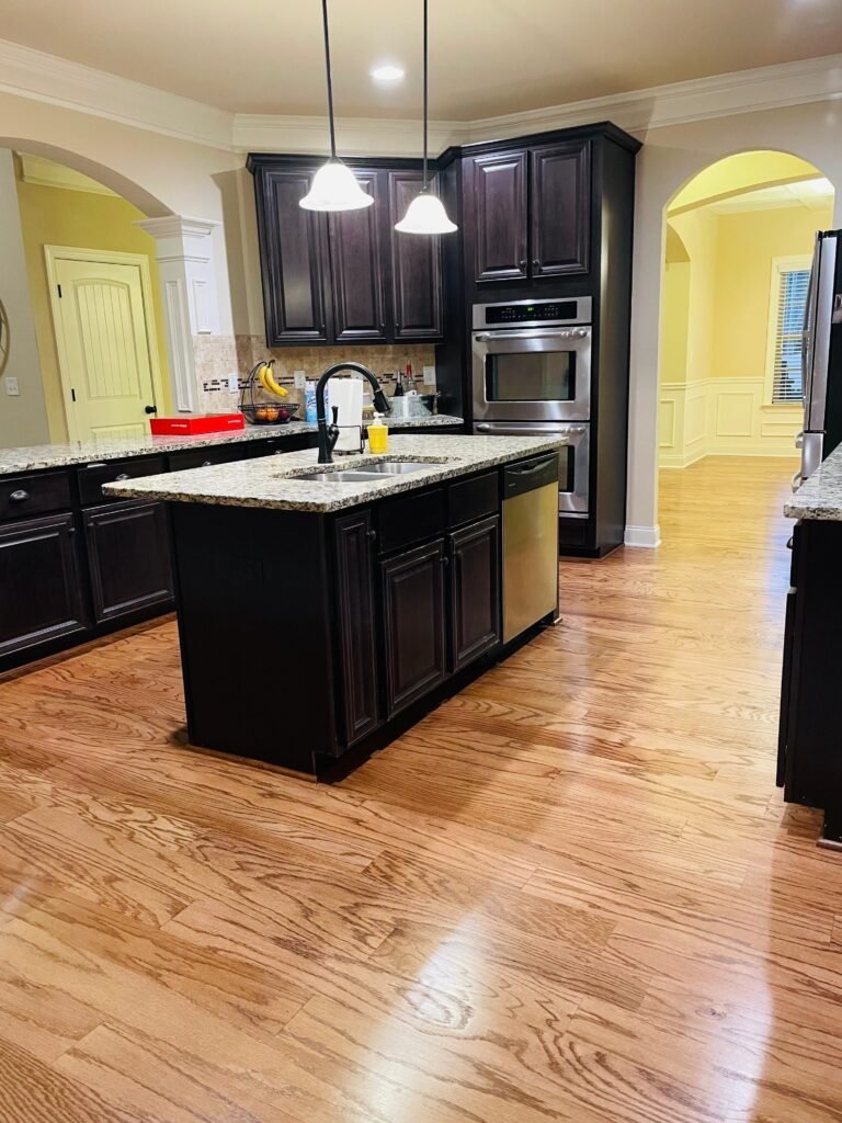 Warm hardwood floor beside a dark cabinet kitchen island